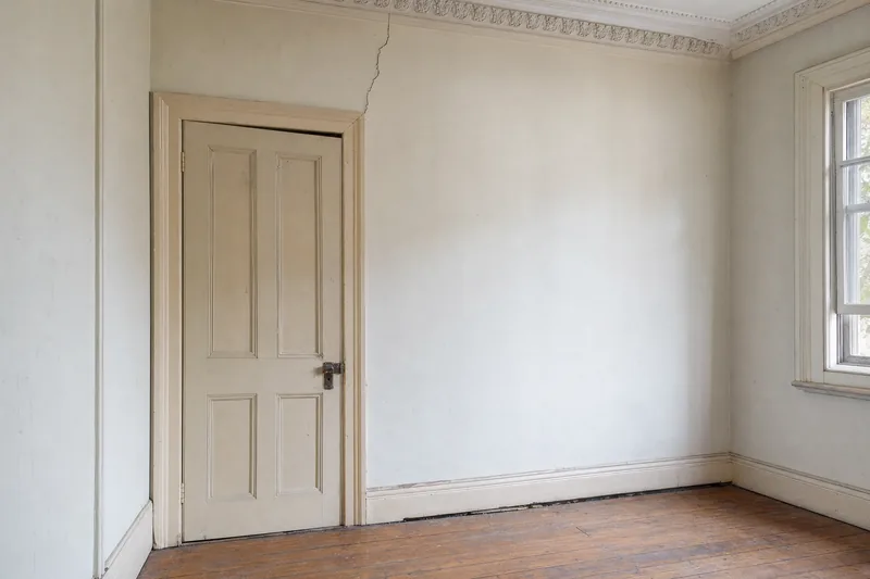 A painted timber door in a plaster wall with a crack rising from its frame to the ceiling cornice — foundation repair, Sydney. Illustrative example.