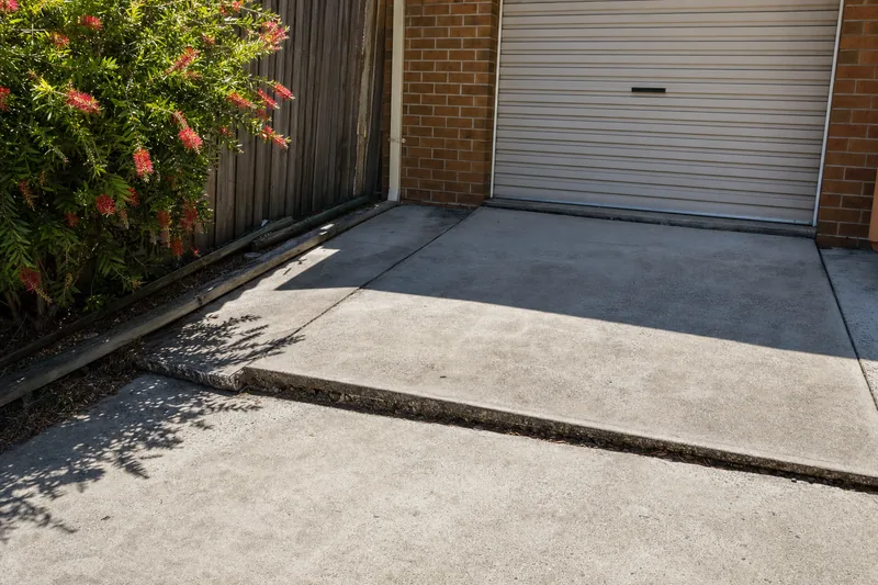 Two concrete driveway slabs meeting at a stepped, open joint in front of a garage door — house levelling, Sydney. Illustrative example.